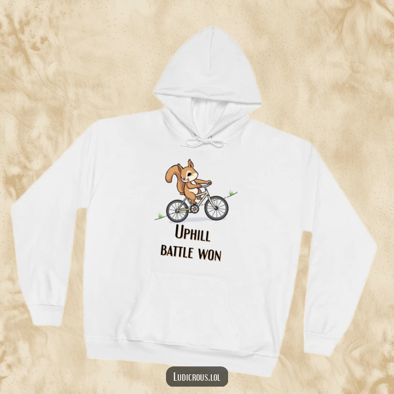 Funny, determined squirrel furiously pedaling uphill on a tiny bicycle, featured on a soft, warm hoodie for ultimate cozy motivation.